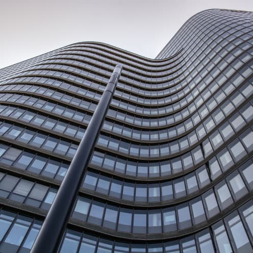 Tall glass high-rise building viewed from below with curving architecture and a lamppost.