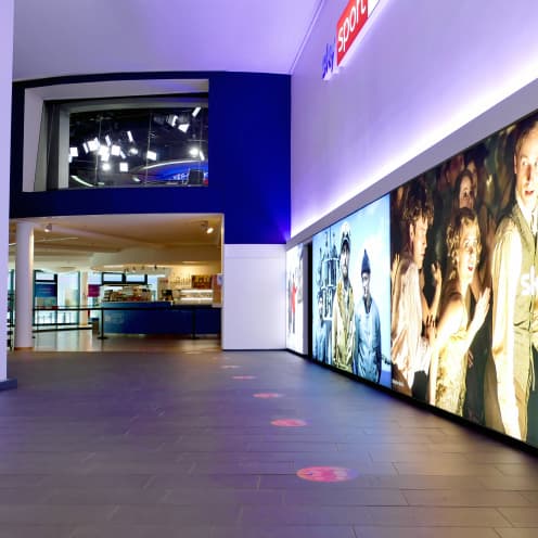 Sky hallway lit by glowing display panels featuring entertainment content and sports.